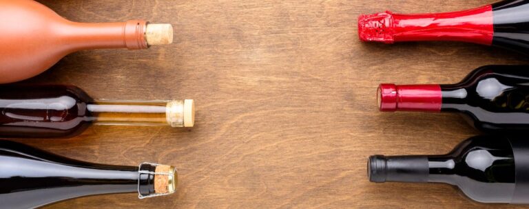 Diferentes tipos de botellas de vino vistas desde arriba, con distintos formatos, colores de vidrio y cierres sobre fondo de madera.