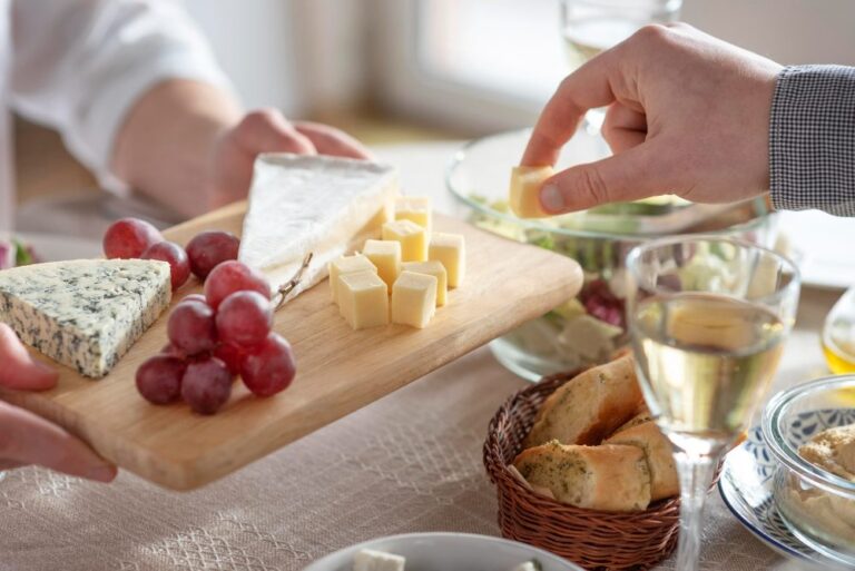 Tabla de quesos con brie, queso azul y gouda acompañada de copa de vino en una mesa en casa