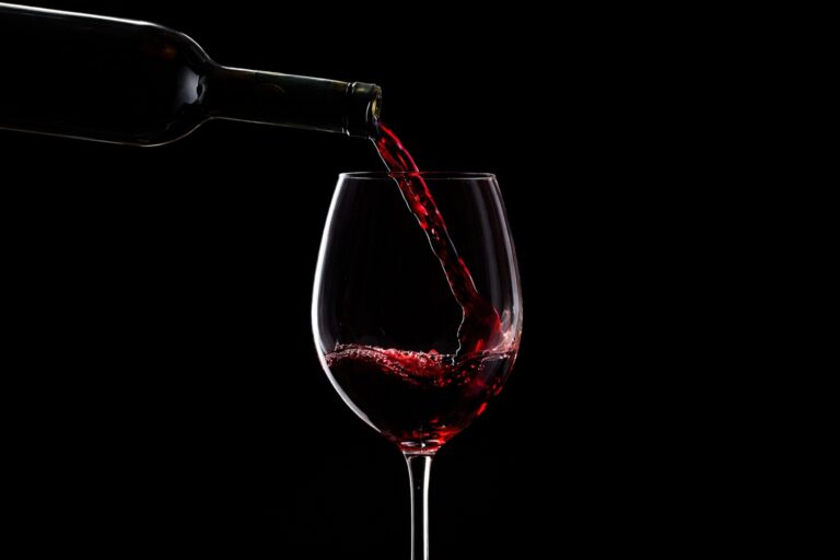 Vino Malbec siendo servido en copa de vino tinto sobre fondo oscuro