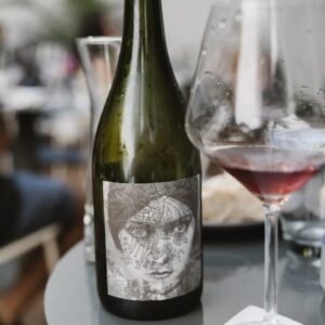 Botella de vino tinto Ver Sacrum Gloria Swan junto a una copa servida, en la mesa de un restaurante o evento.