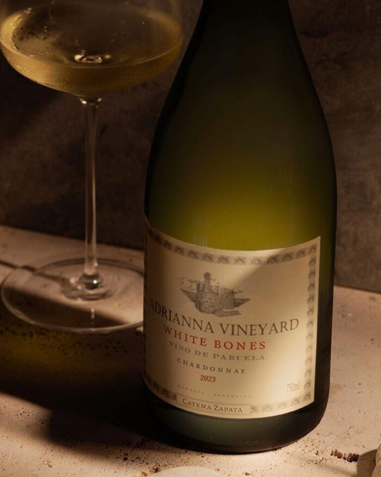 Botella de Chardonnay Adrianna Vineyard White Bones junto a una copa servida a temperatura de servicio.