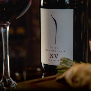 Primer plano de una botella de vino Pulenta Gran Pinot Noir XV 2020 con una copa de vino servida al lado.