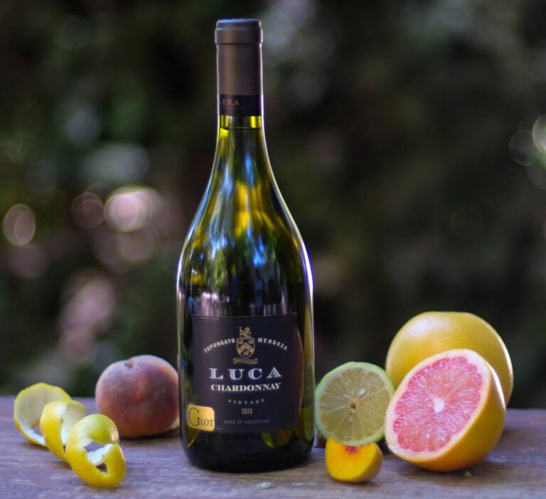Botella de Luca Chardonnay G Lot, vino blanco de Gualtallary, Mendoza, acompañada de duraznos, pomelo y cítricos sobre una mesa.